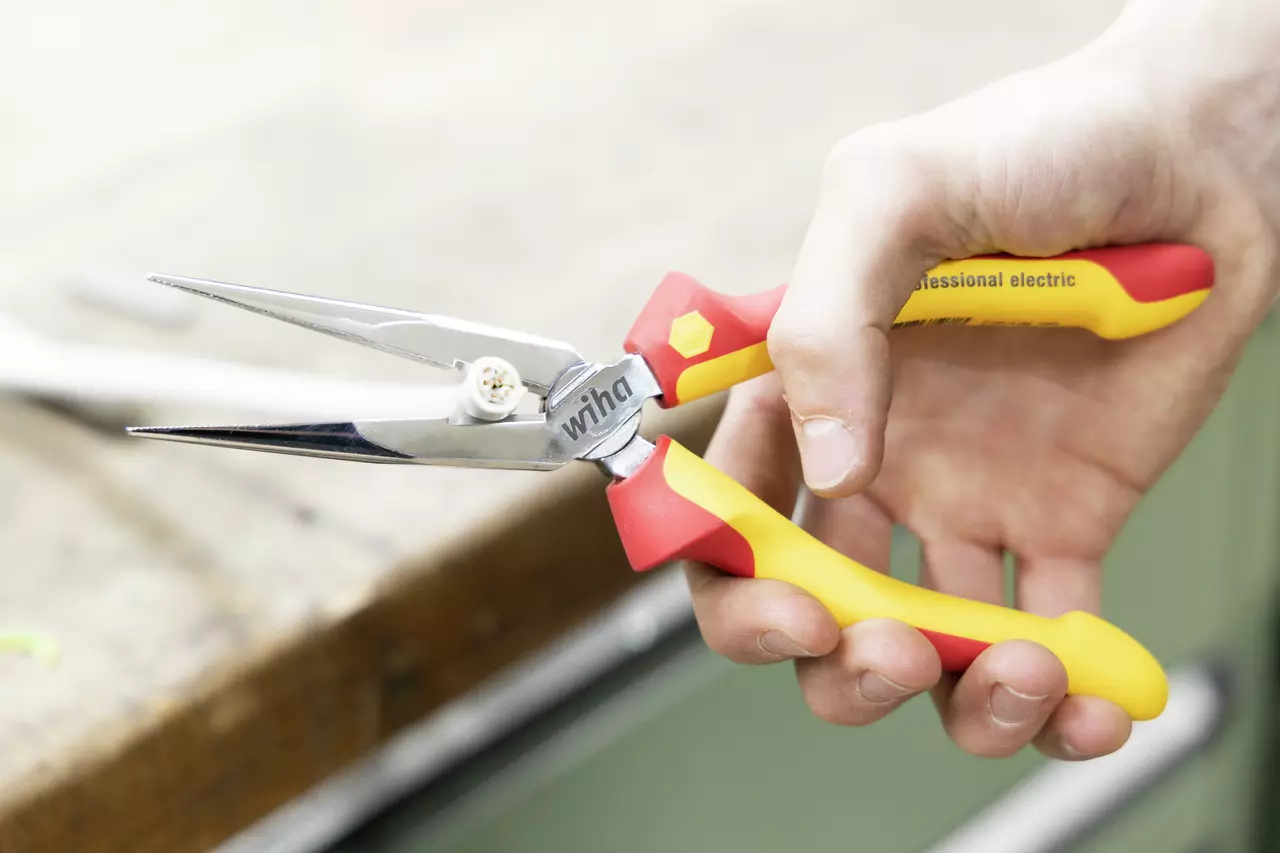 A hand holding red and yellow needle-nose pliers gripping a small wire piece.