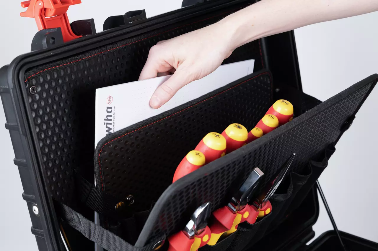 A hand placing a document into a black tool case with red and yellow screwdrivers visible.
