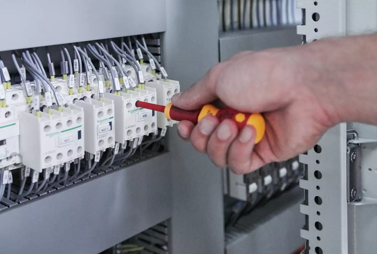 Person using an electric screwdriver on a control panel with wires.