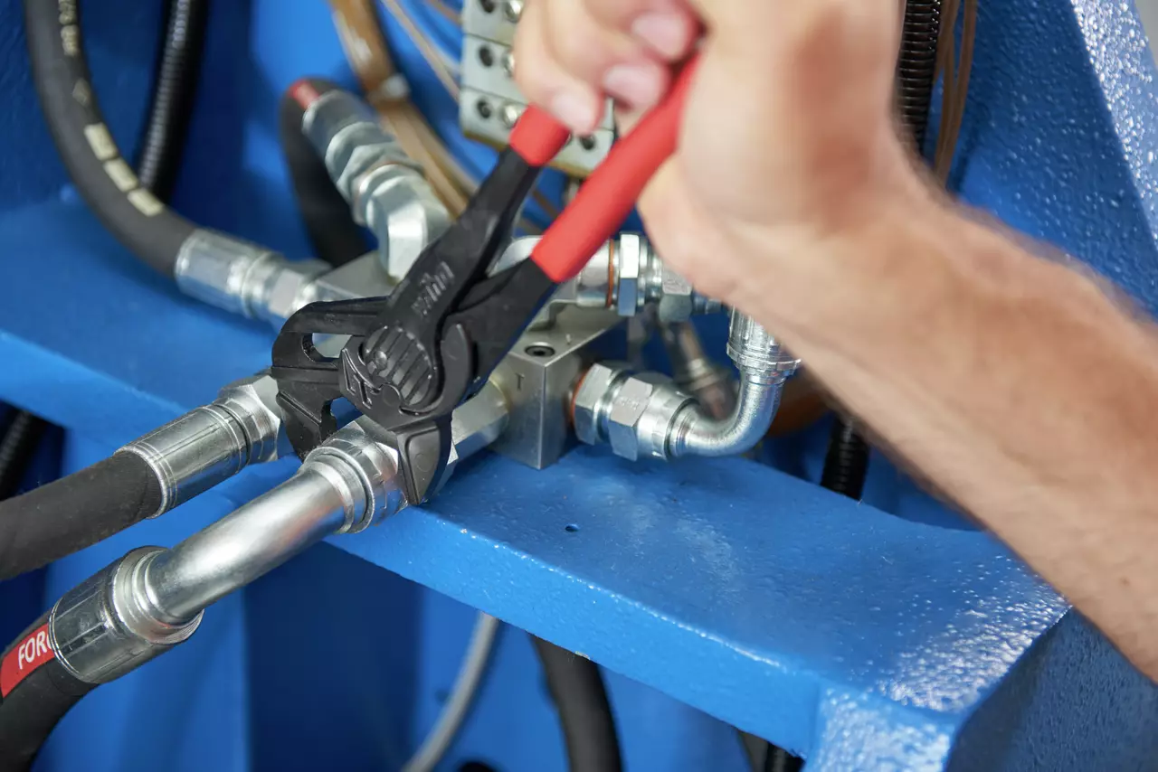 Ruka používá kleště na kovové armatuře s červenými rukojeťmi v mechanickém prostředí.