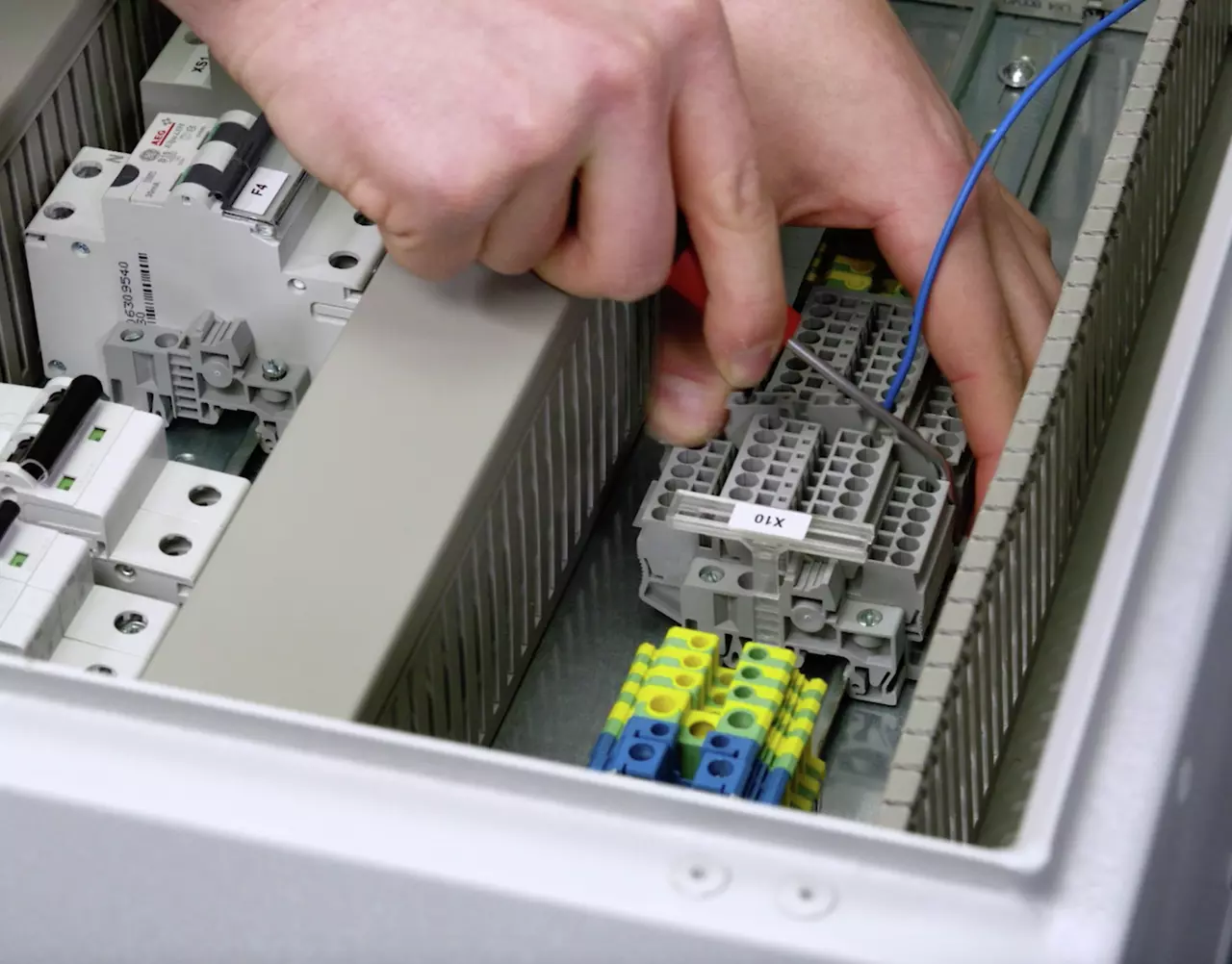 A person uses a tool to connect wires in an electrical panel.