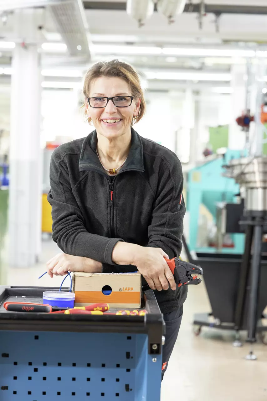 A person in work attire stands by a workshop cart with tools and a wire stripping tool.
