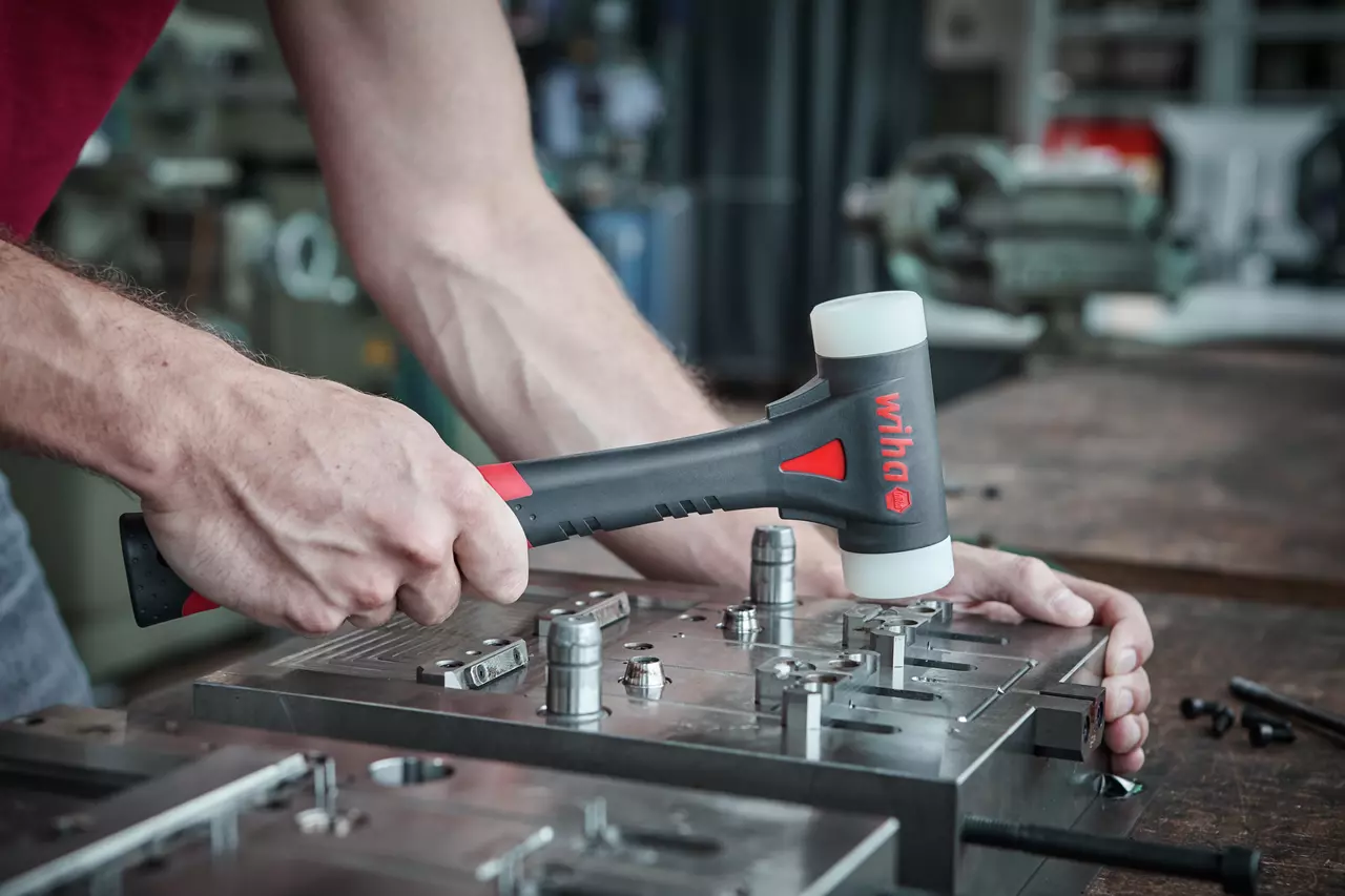 Person using rubber mallet on metal workpiece in workshop