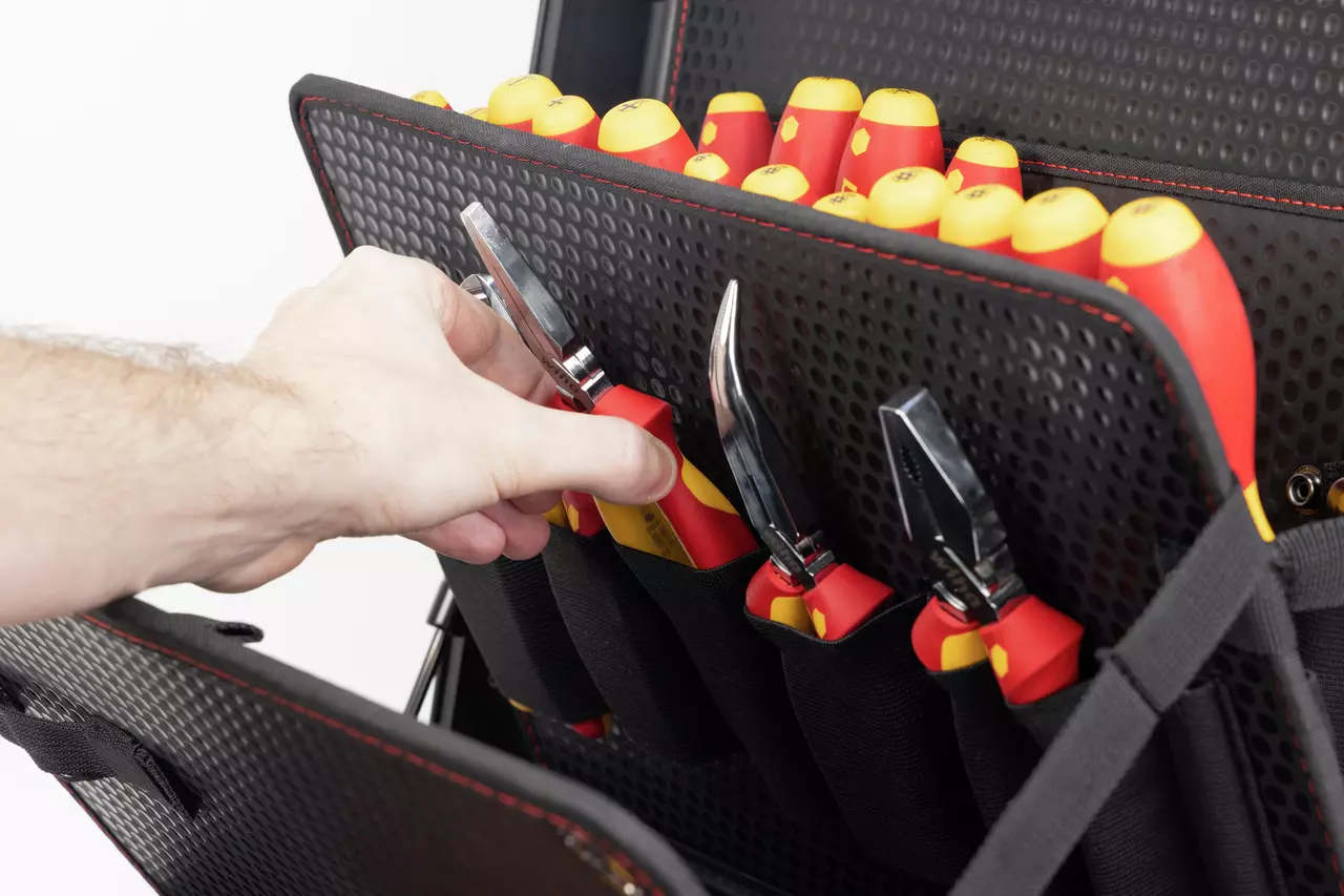 A person selects a tool from a case filled with red and yellow-handled tools.