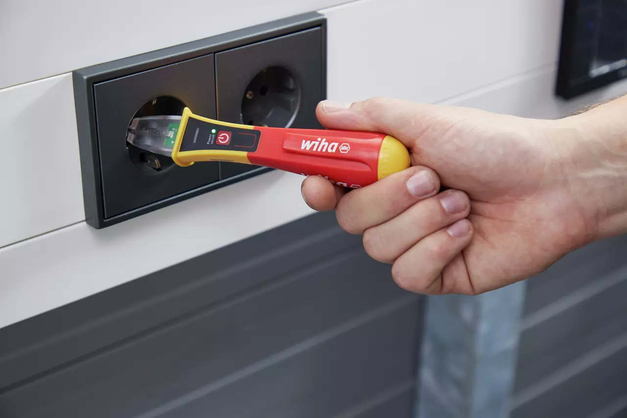 Hand using non-contact voltage detector in power outlet