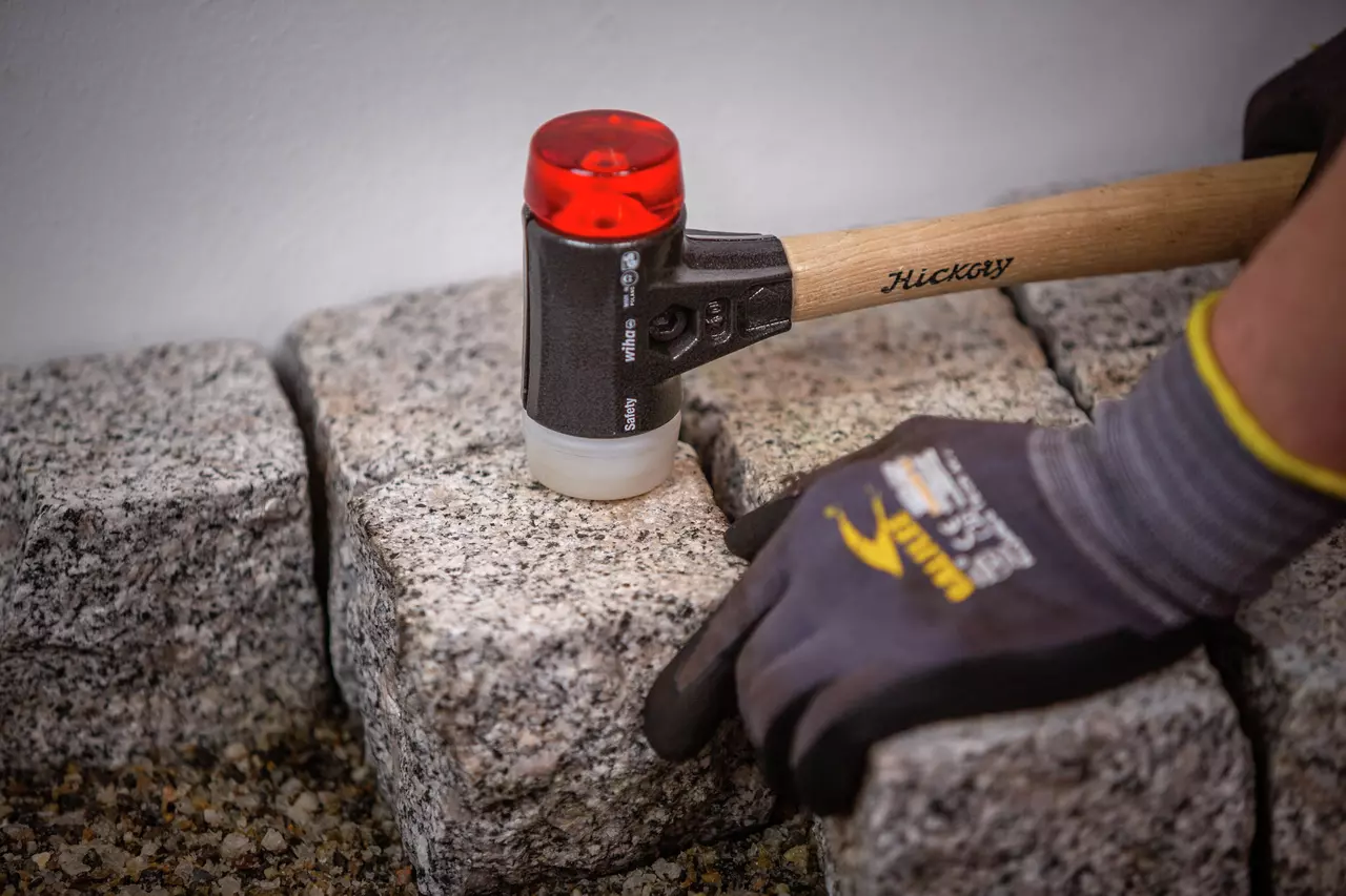 A person using a mallet with a wooden handle and rubber head to adjust stone pavers.