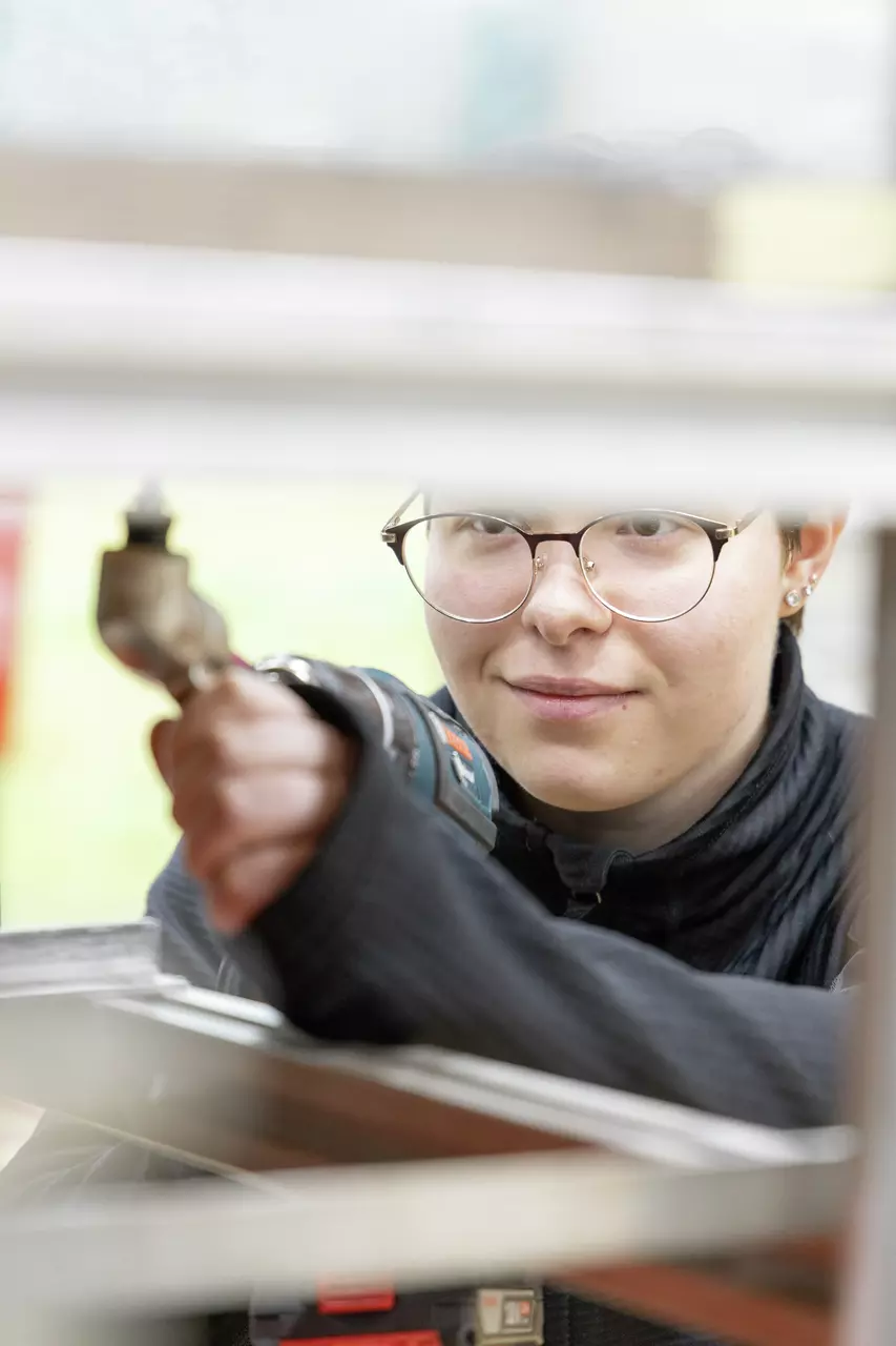 Person with glasses using a cordless drill on a metal structure.