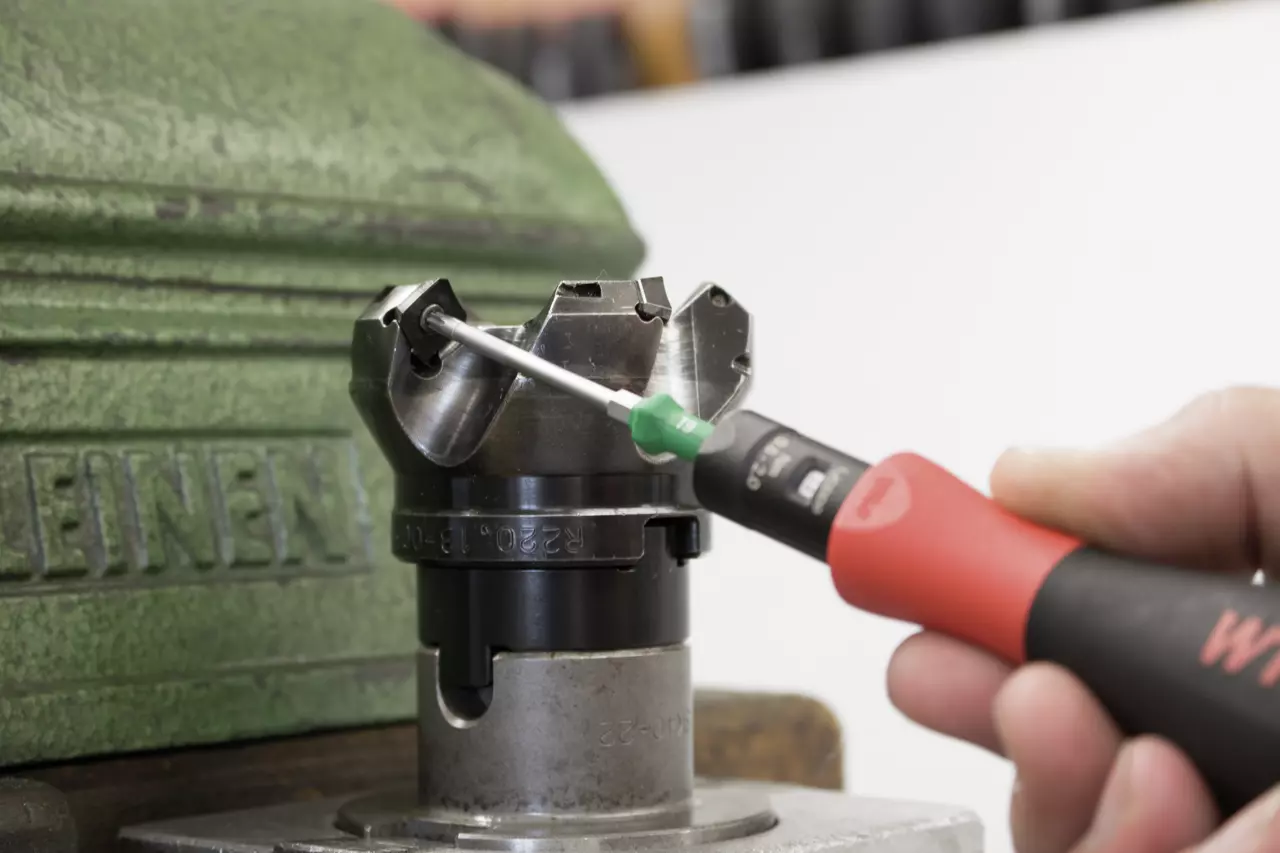 A person uses a torque screwdriver on a metal component in a green vise.