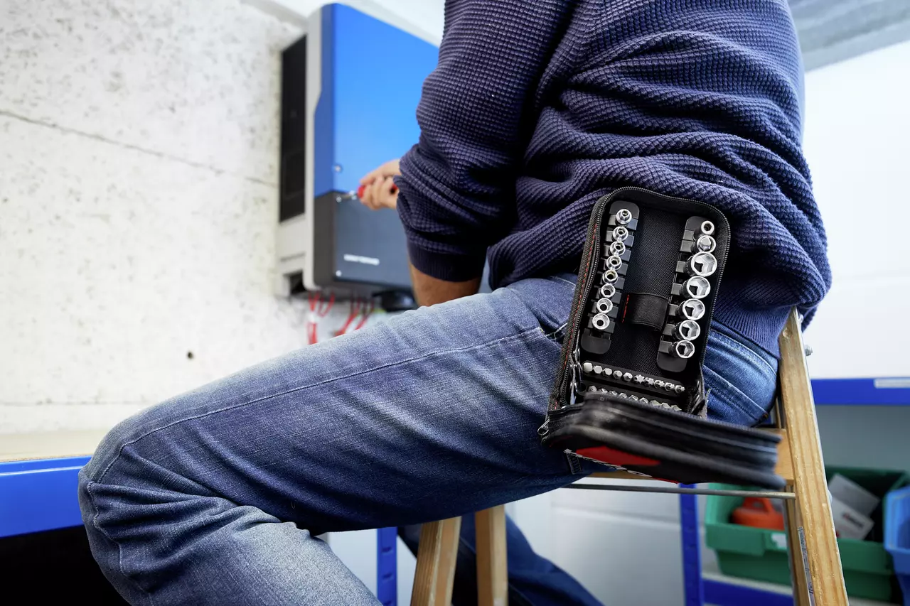 Person working with a socket set on a wall-mounted device