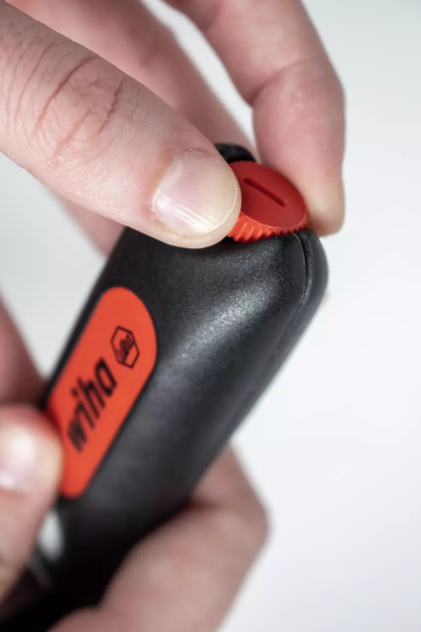 Close-up of a hand holding a black stripping tool with a red dial.