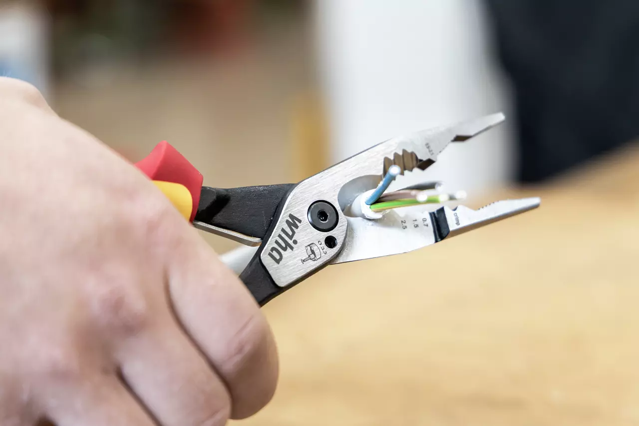 Hand houdt combinatietang met rode en gele handvatten die draden vastgrijpt.