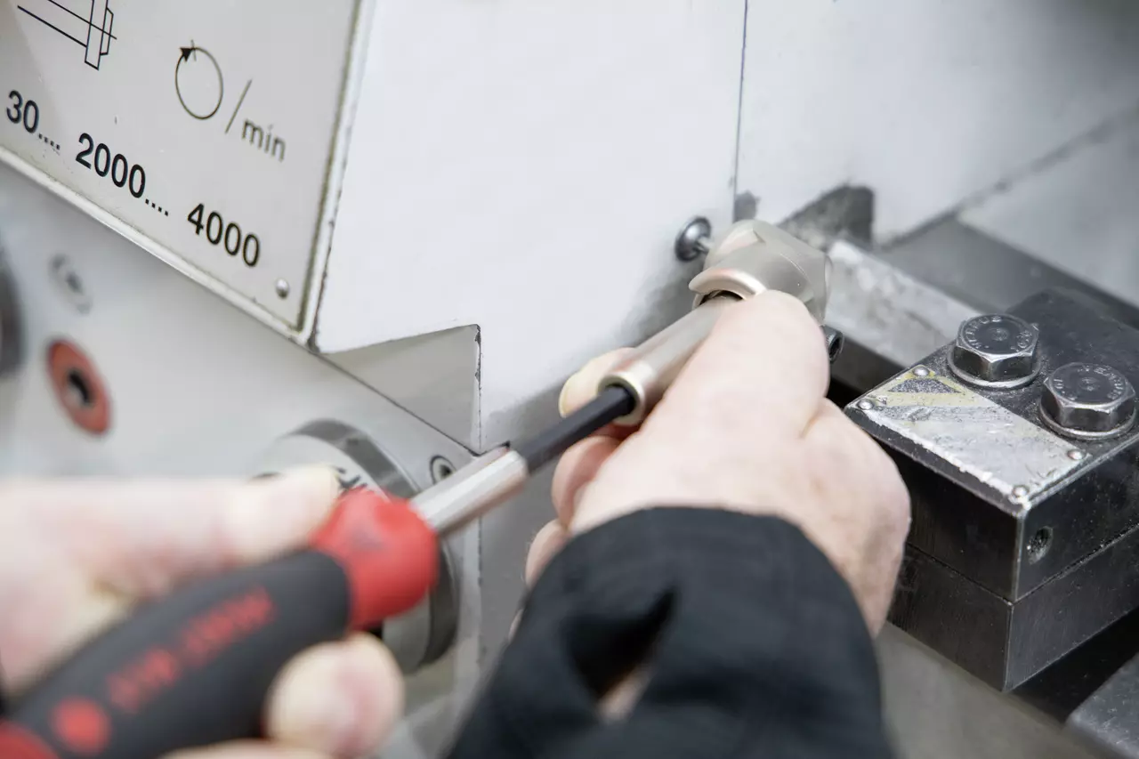 Person using an electric screwdriver on a machine.