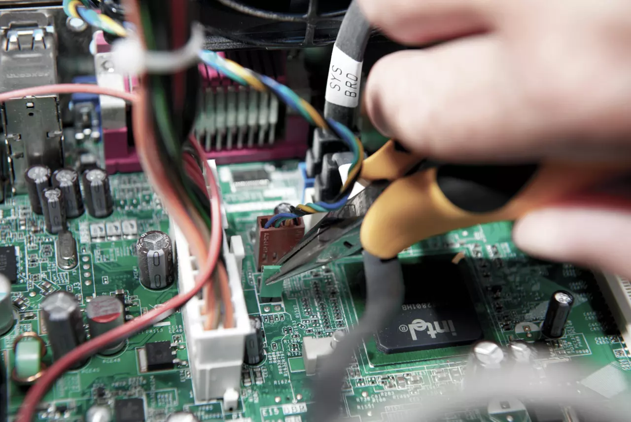 A hand holds needle-nose pliers working on a computer circuit board.