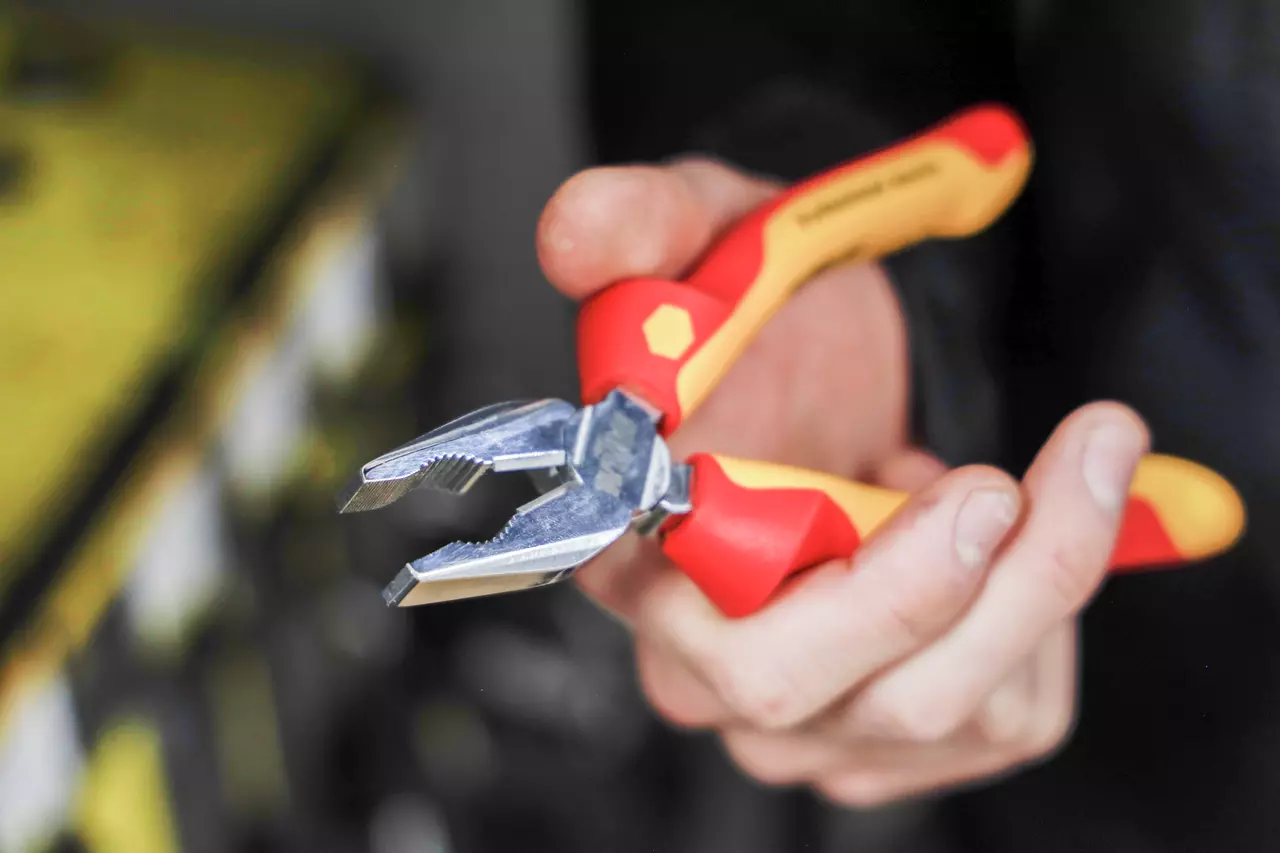 A person holding a red and yellow pliers with metal jaws.
