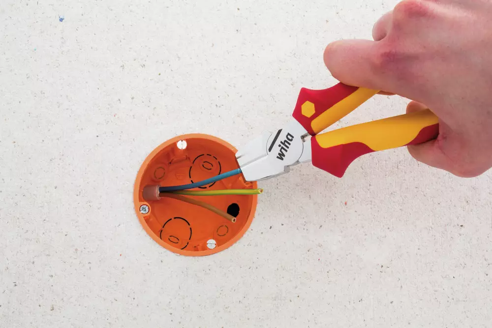 A hand using pliers to strip wires in an orange electrical box.
