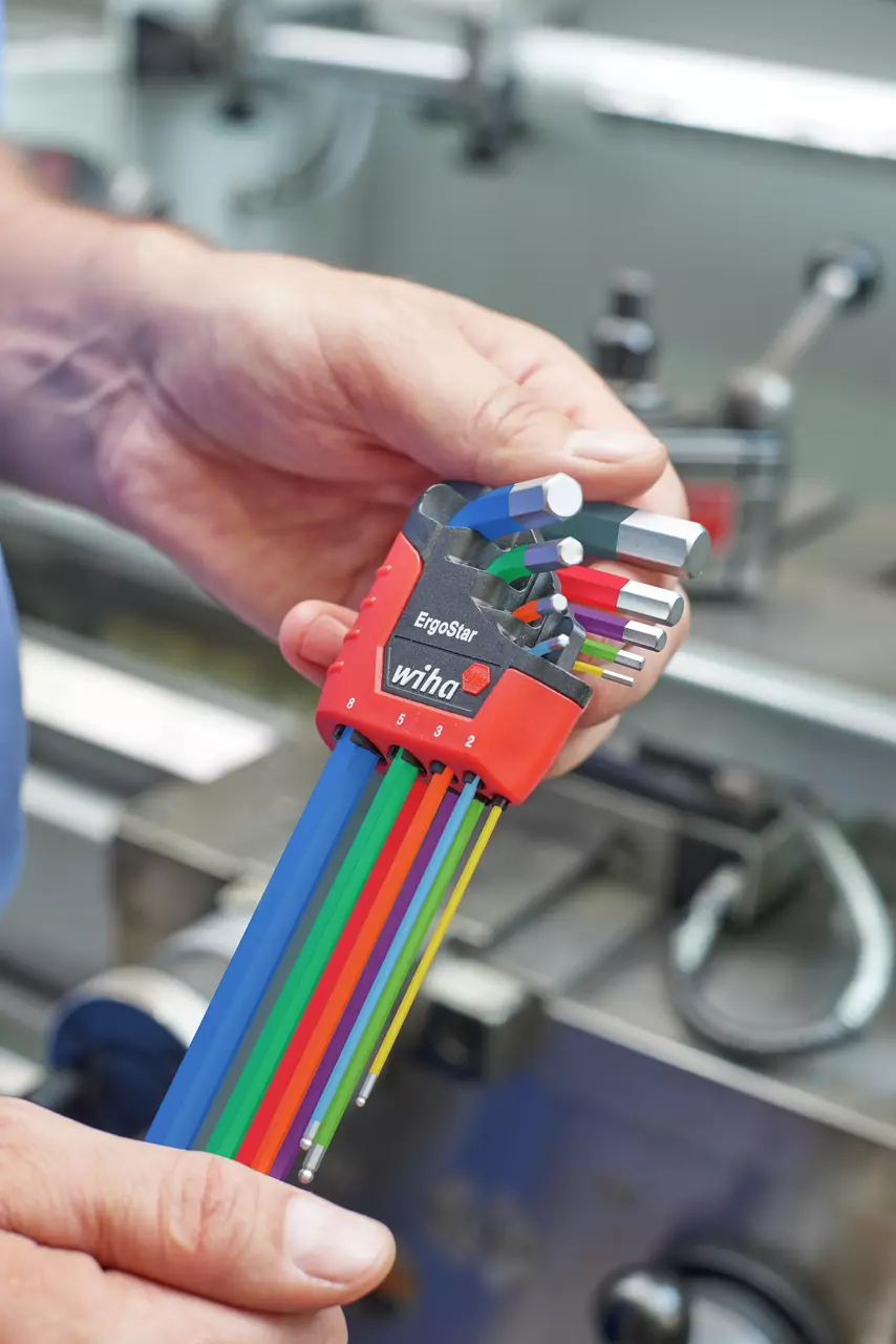 A person holds a set of colorful L-shaped hex keys in a red holder labeled "ErgoStar" in a workshop.