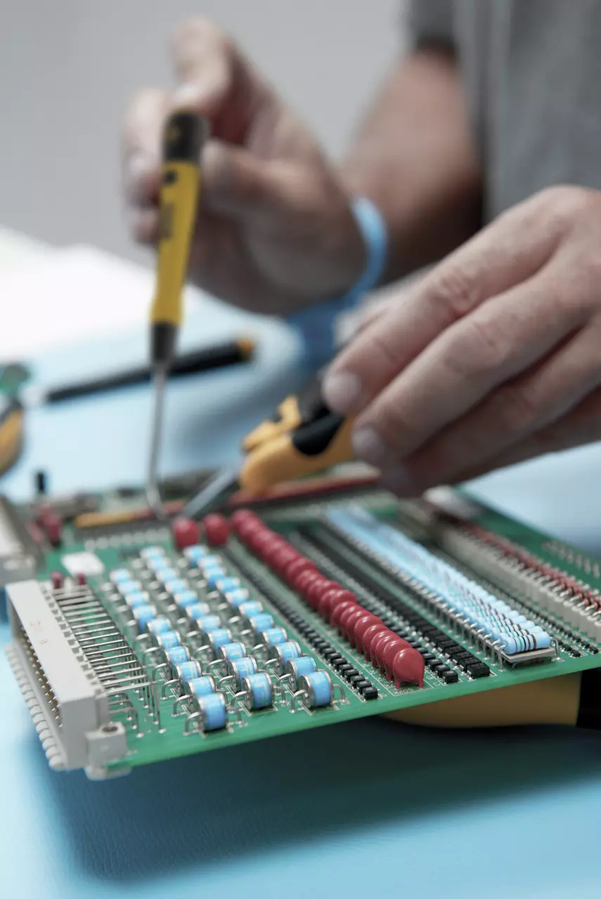 Person using tools on a circuit board with colored components.