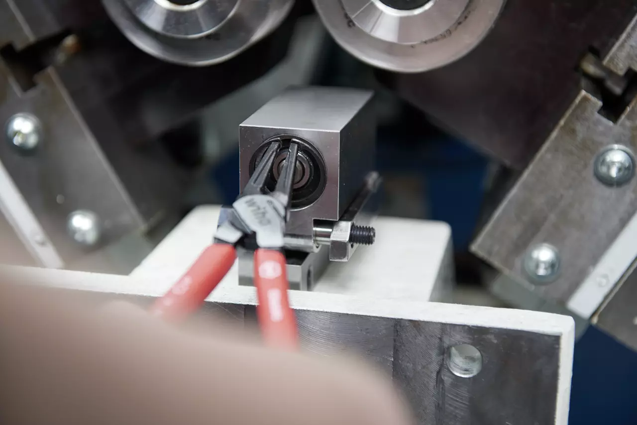 Pliers gripping a retaining ring inside a metal component with machinery in the background.