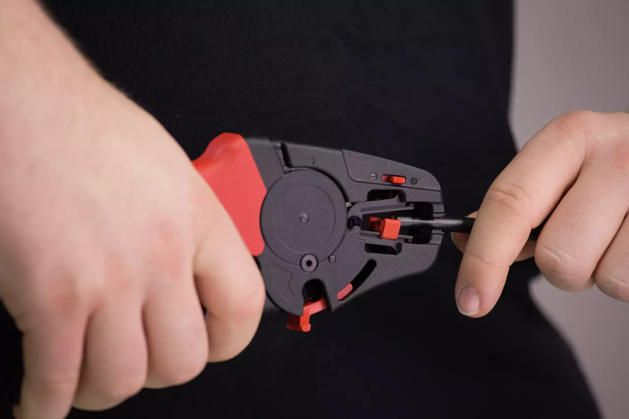 Person using an automatic wire stripper on a black cable