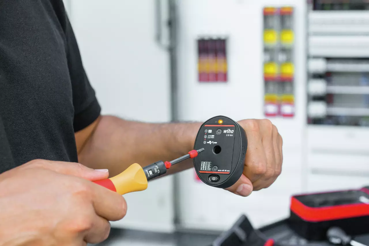 A person using a torque tester with a screwdriver in a workshop setting.
