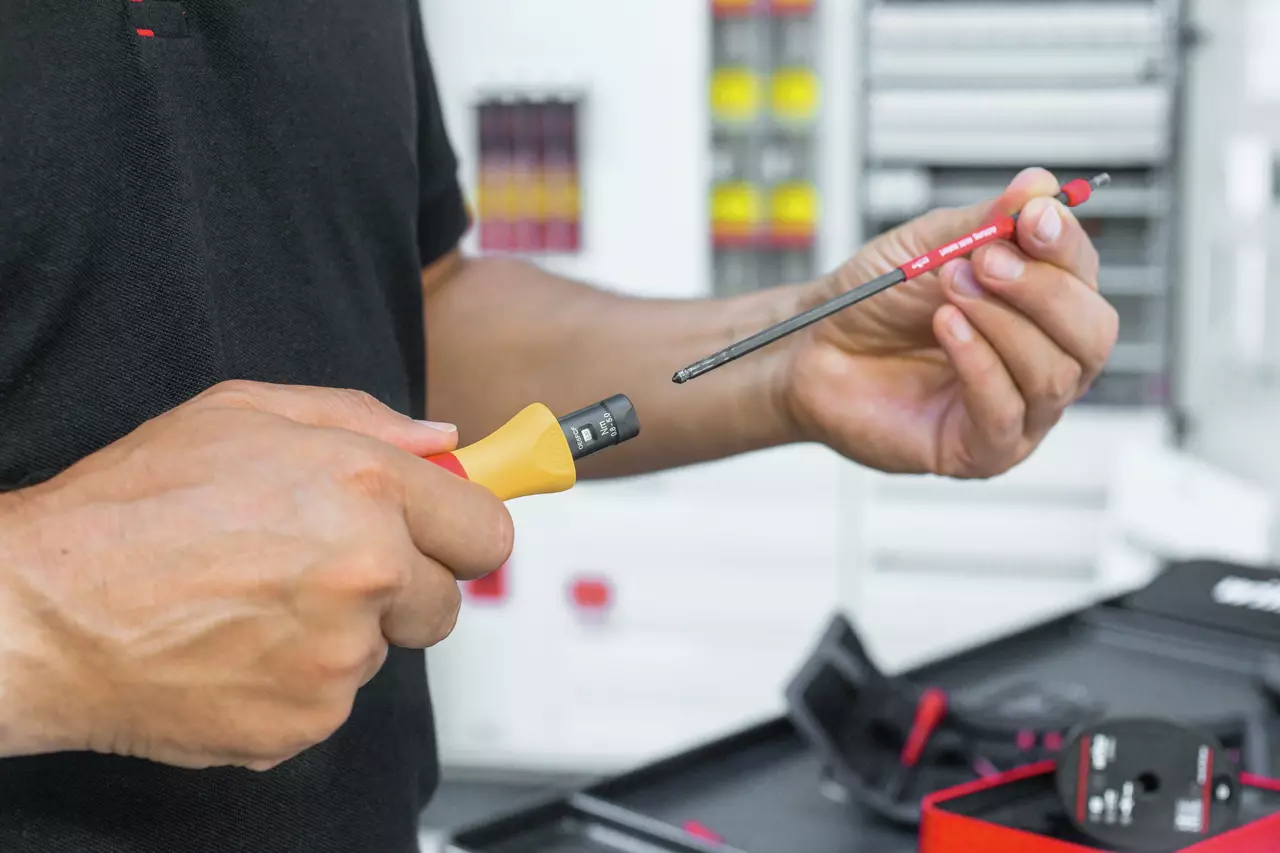 Person holding a yellow handle and a red screwdriver bit, preparing to attach them.