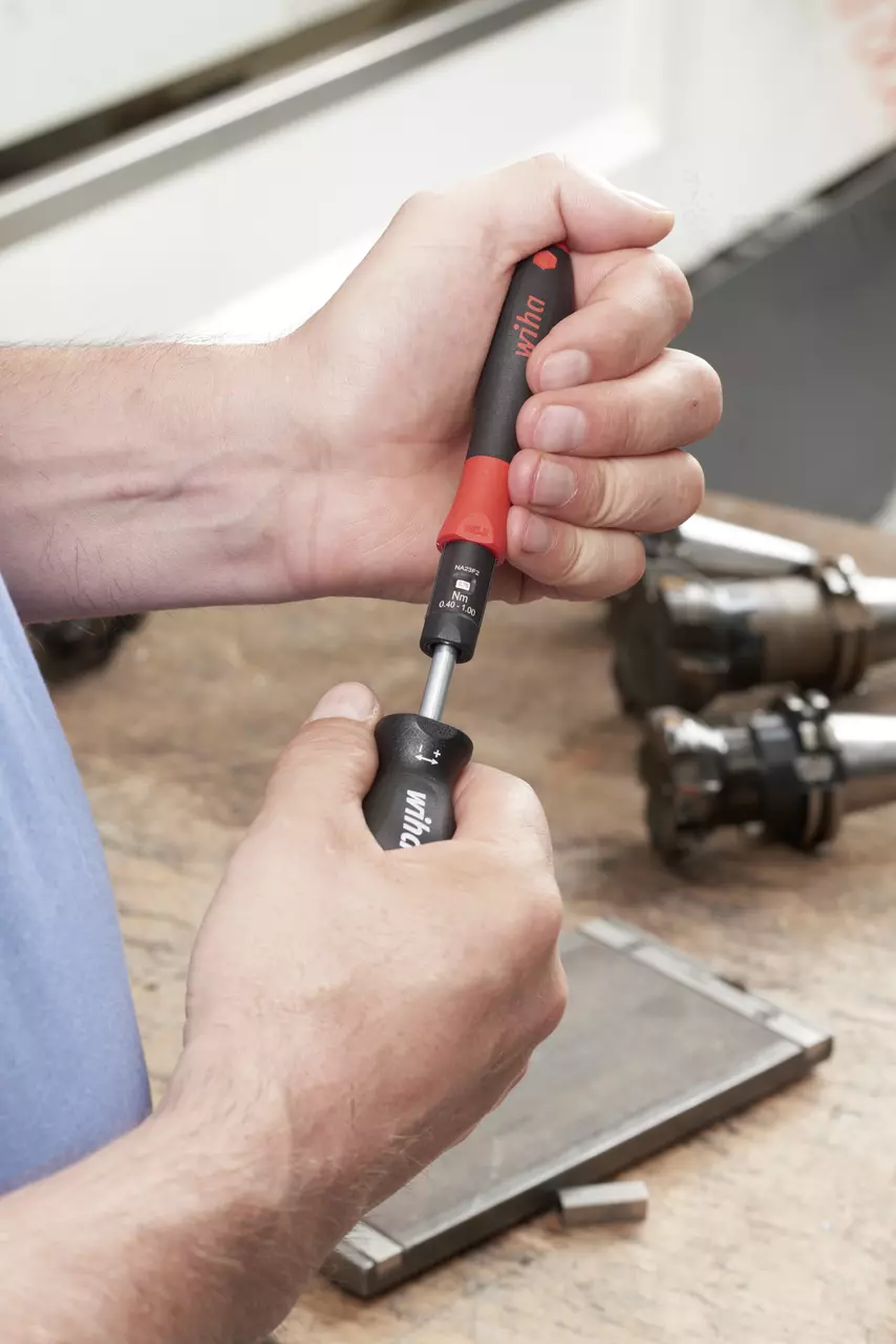 Person adjusting a torque screwdriver on a workbench.