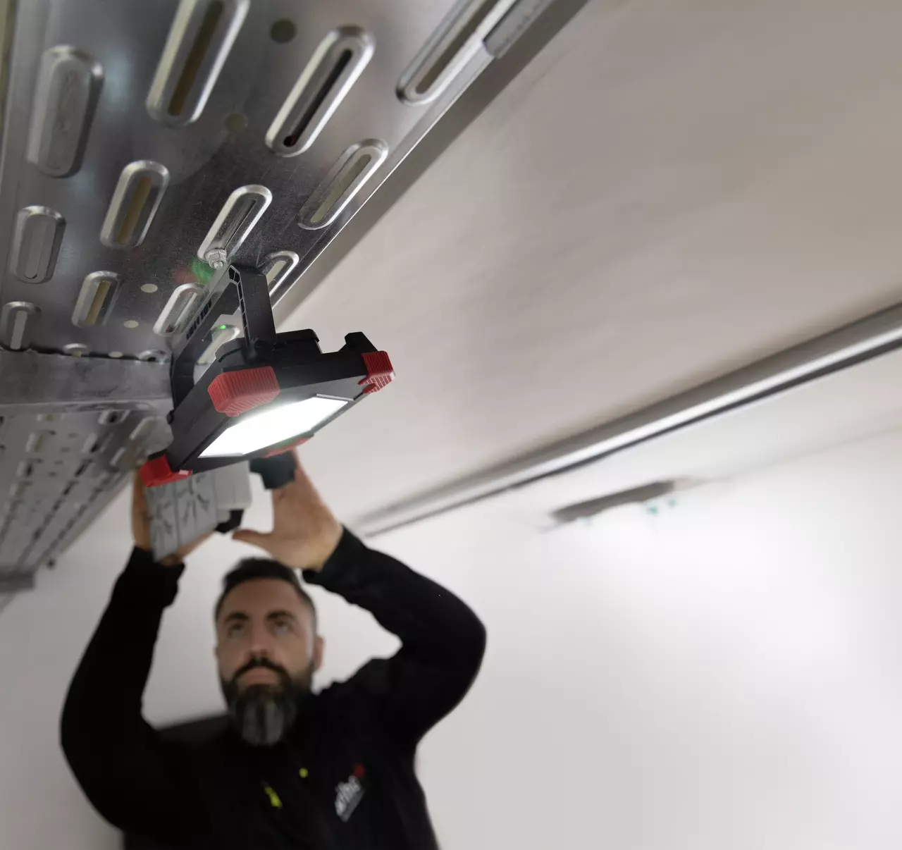 A person is adjusting a work light on a metal structure ceiling.