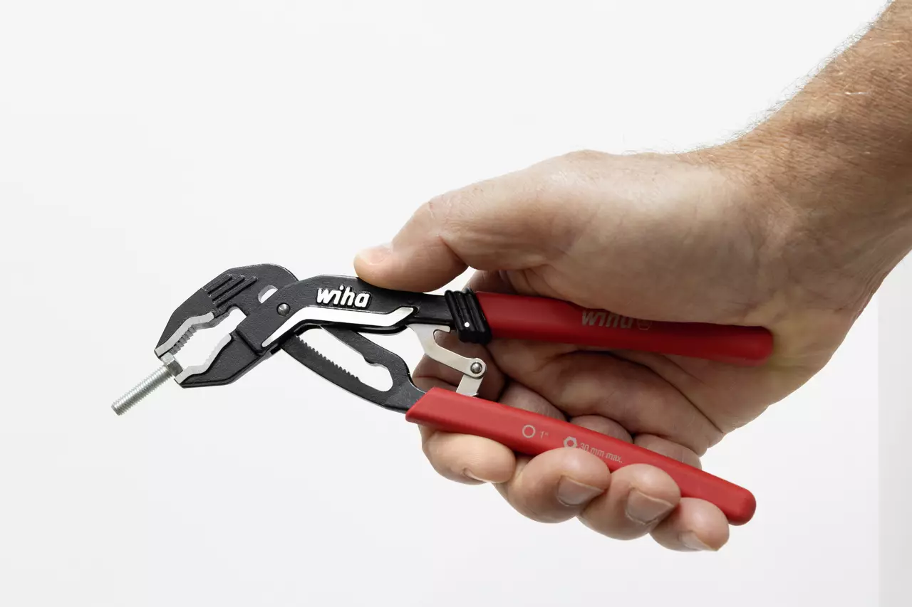 A hand holding red-handled water pump pliers gripping a metal bolt.