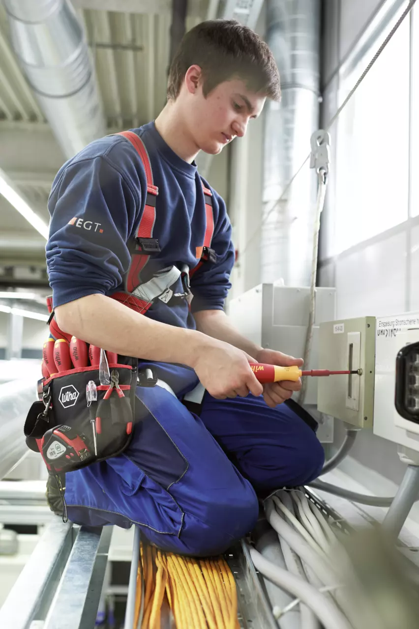 A person is working with an electric screwdriver on a control cabinet.