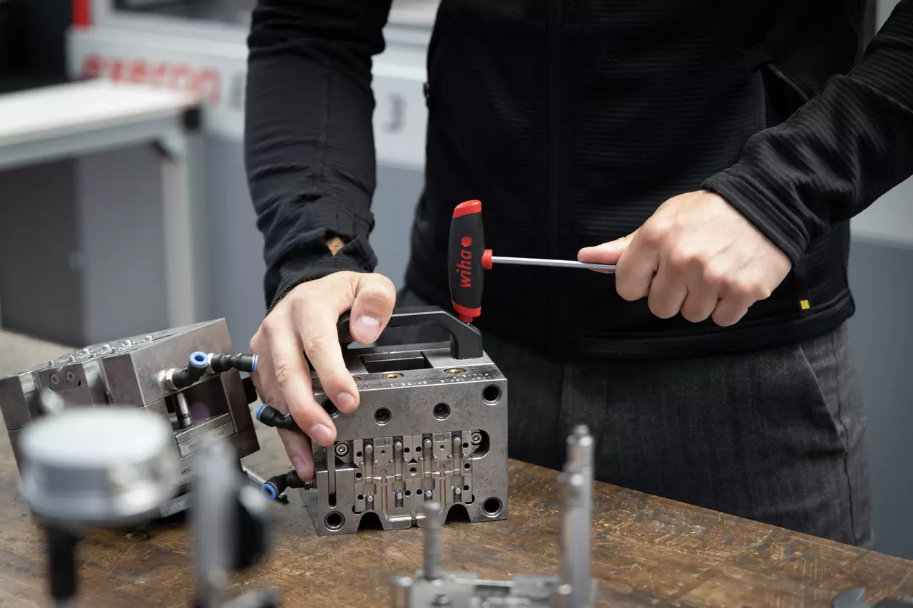 A person uses a T-handle wrench on a metal component at a workbench.