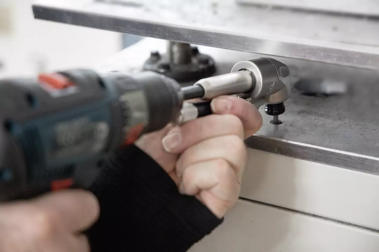 Person using a cordless drill with an angle attachment on a metal surface.