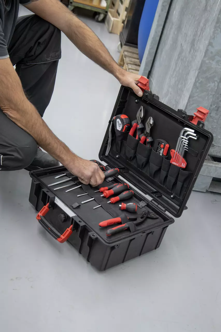 A person kneeling beside an open tool case filled with various hand tools, including screwdrivers and pliers.