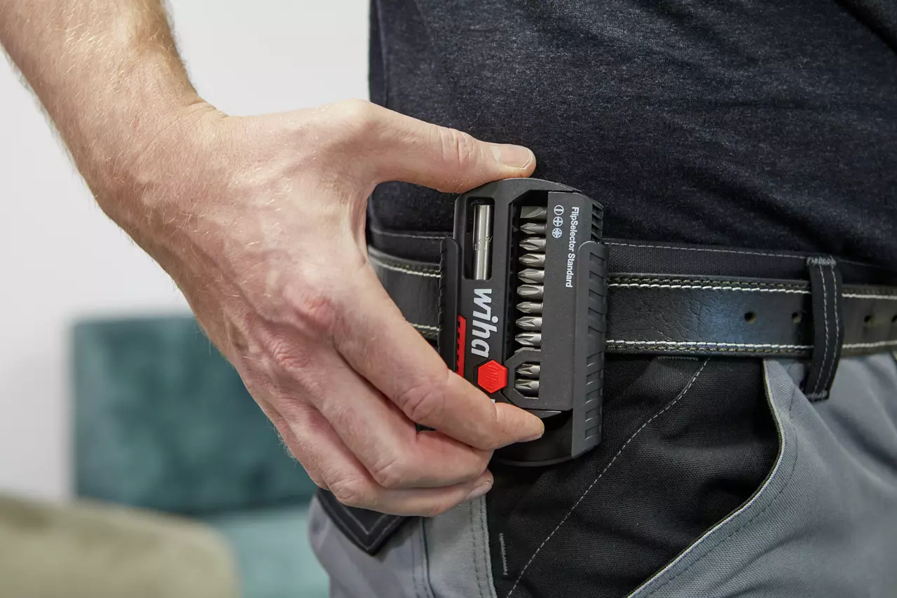A person attaching a black bit holder with multiple bits to their belt.