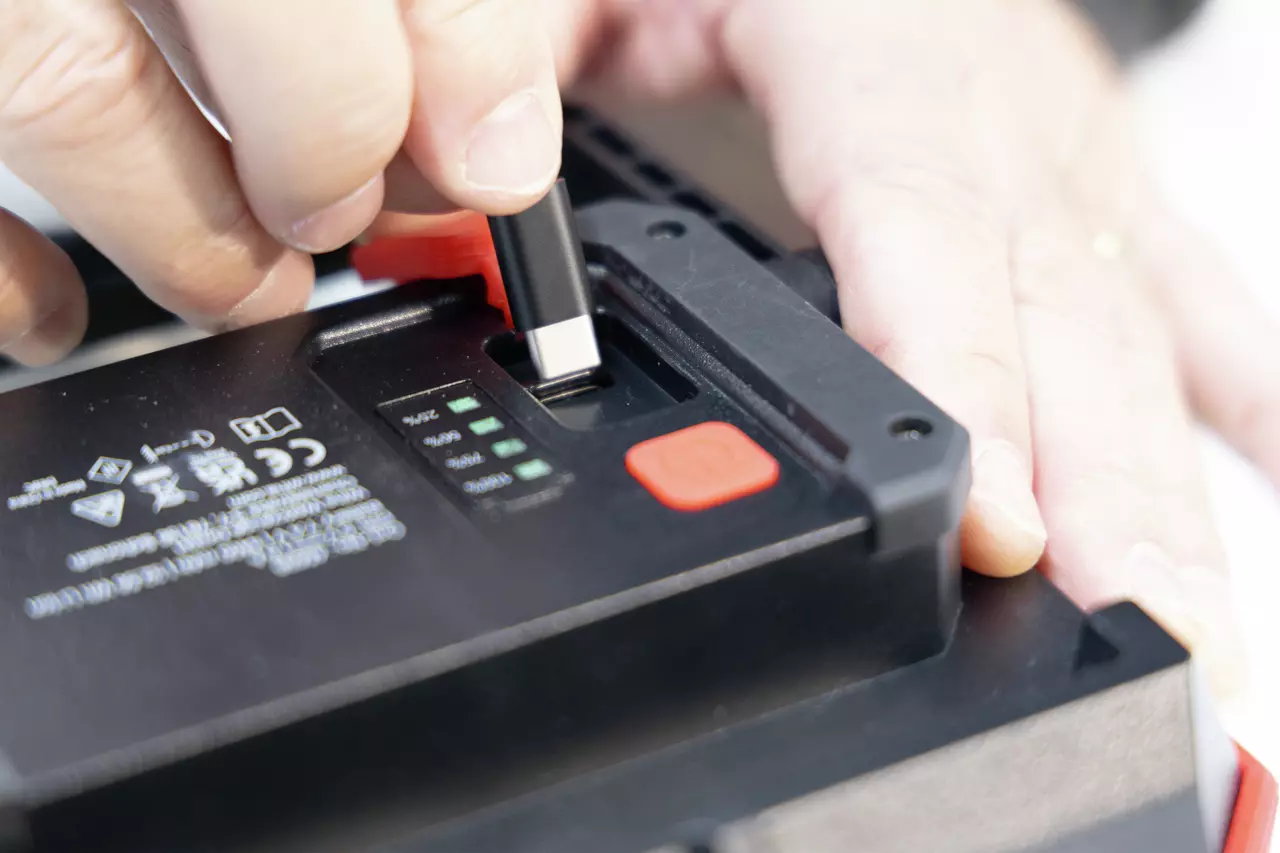 Person inserting USB-C cable into black device with labels and indicators.