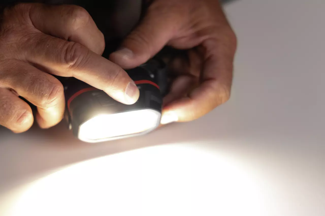 A person holding a bright headlamp, pressing a button. The light is shining on a white surface.