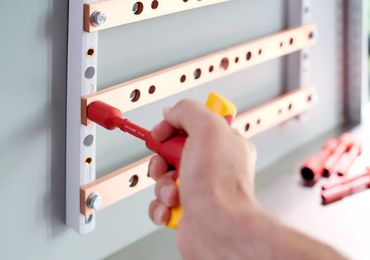 A person uses an insulated screwdriver on a metal frame with copper bars.