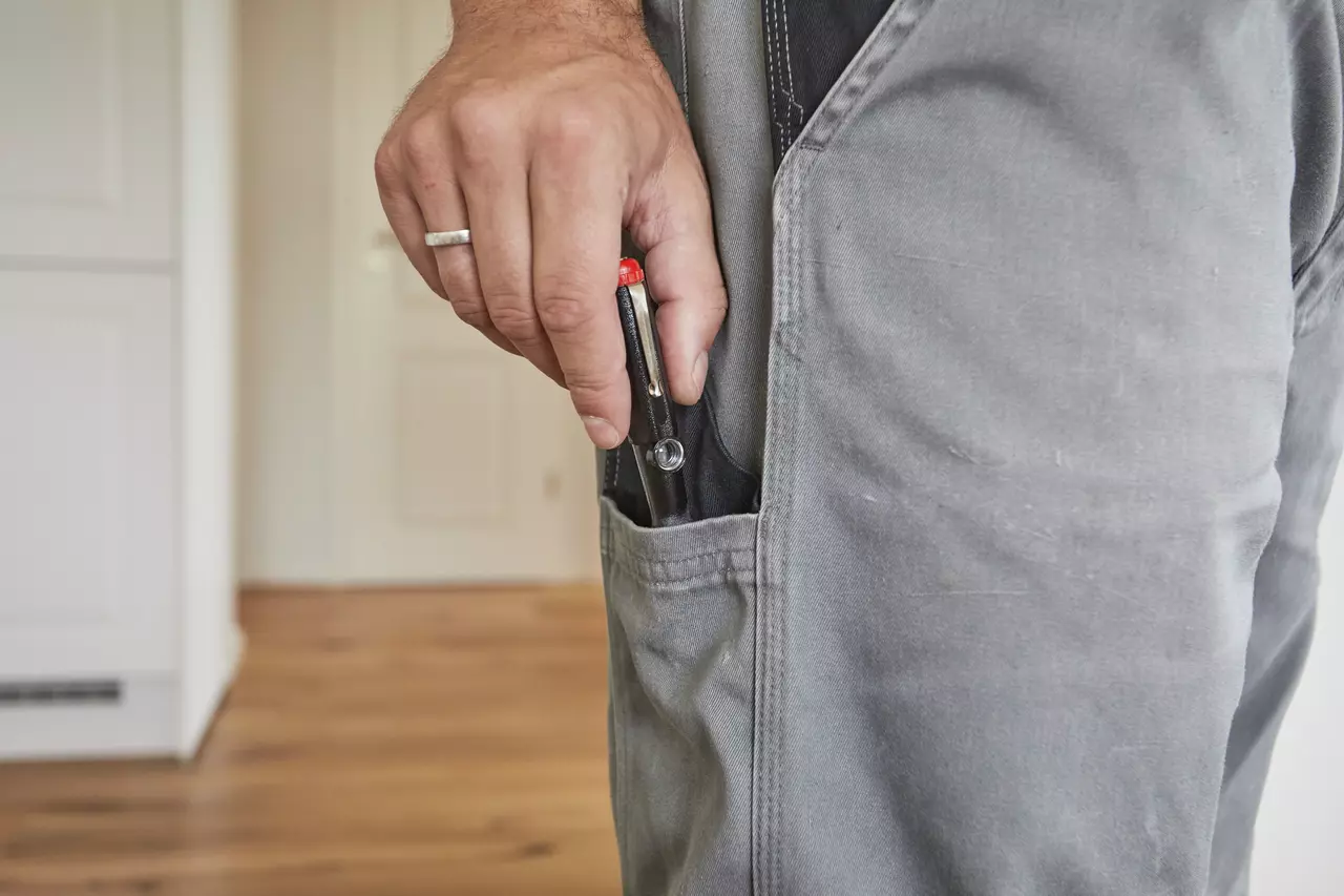 Person placing a voltage tester with a red cap into a gray pants pocket.