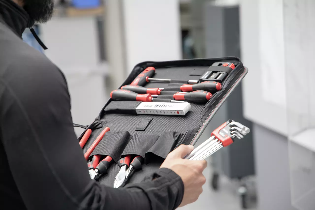 Person holding a tool set with screwdrivers and pliers in a black case.