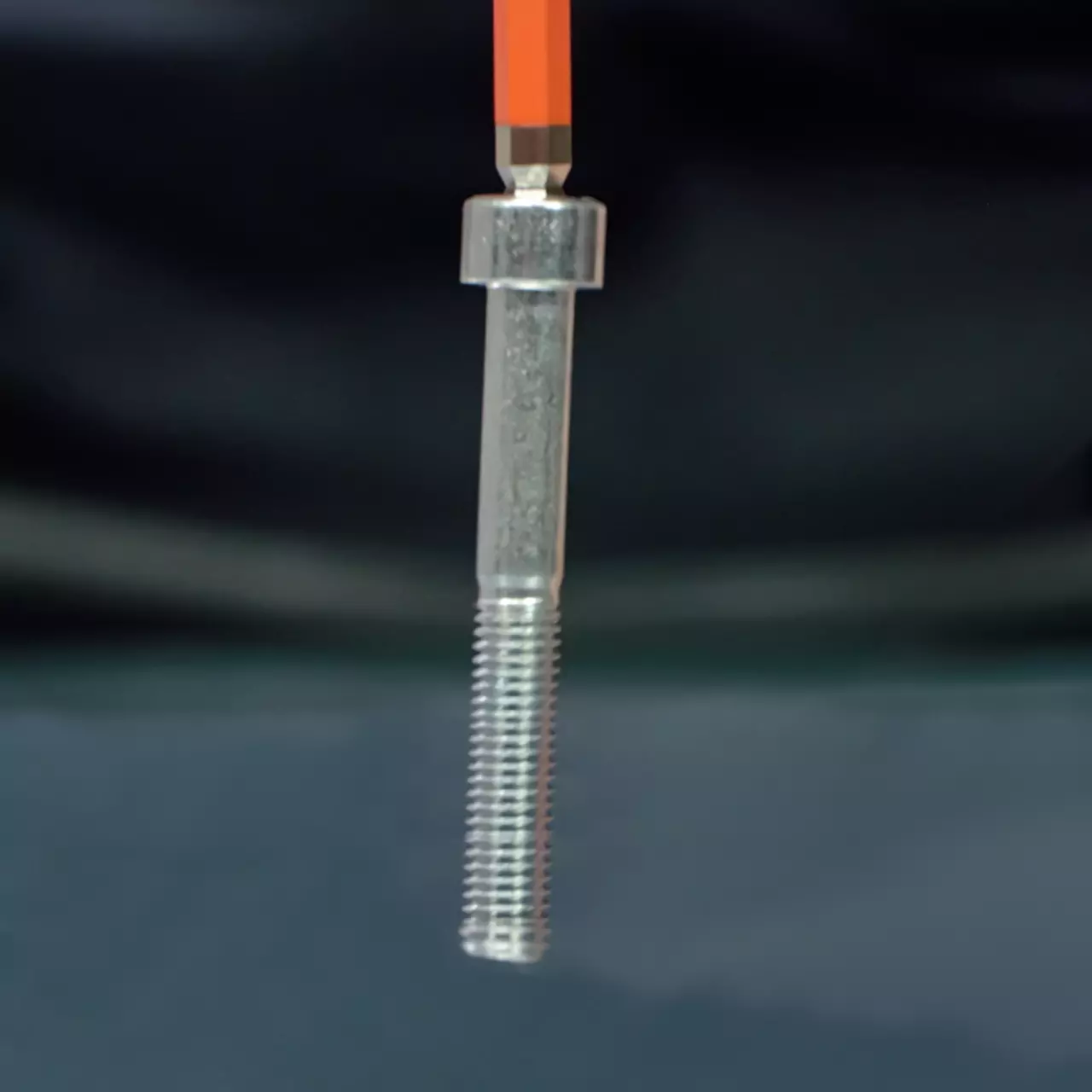 Close-up of a metal hex key inserted into a bolt, with a black background.