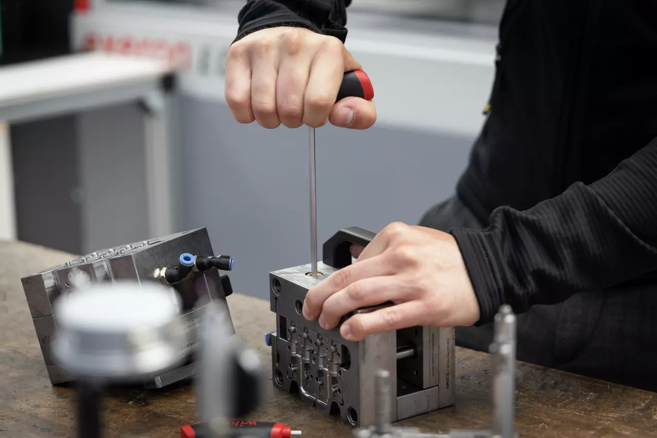 Person using a screwdriver to work on a metal block on a workbench.