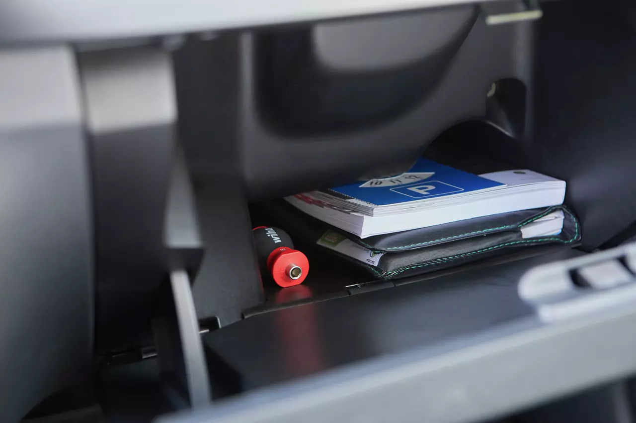 A red-handled screwdriver is in a car glovebox with books and a folder.