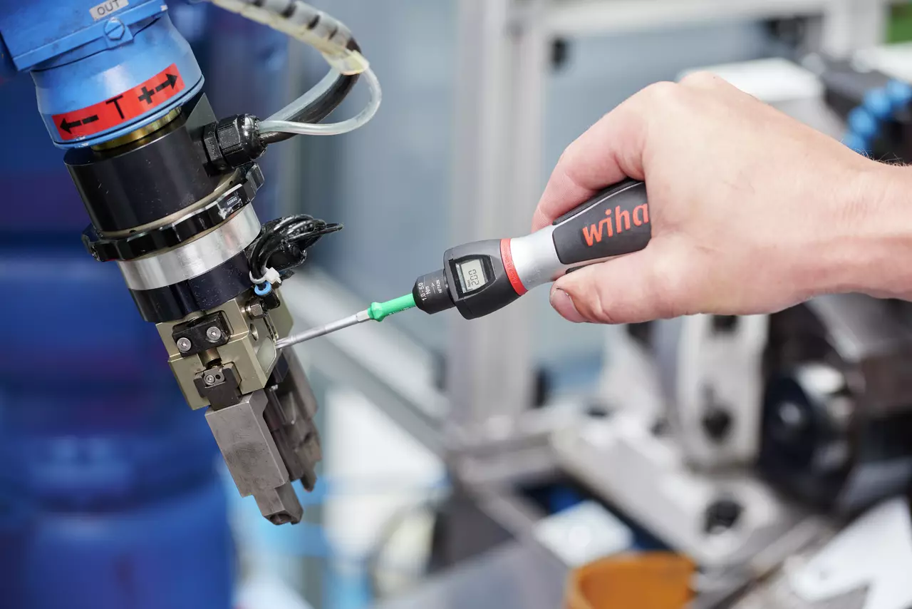 A person uses a digital torque screwdriver on a machine part.