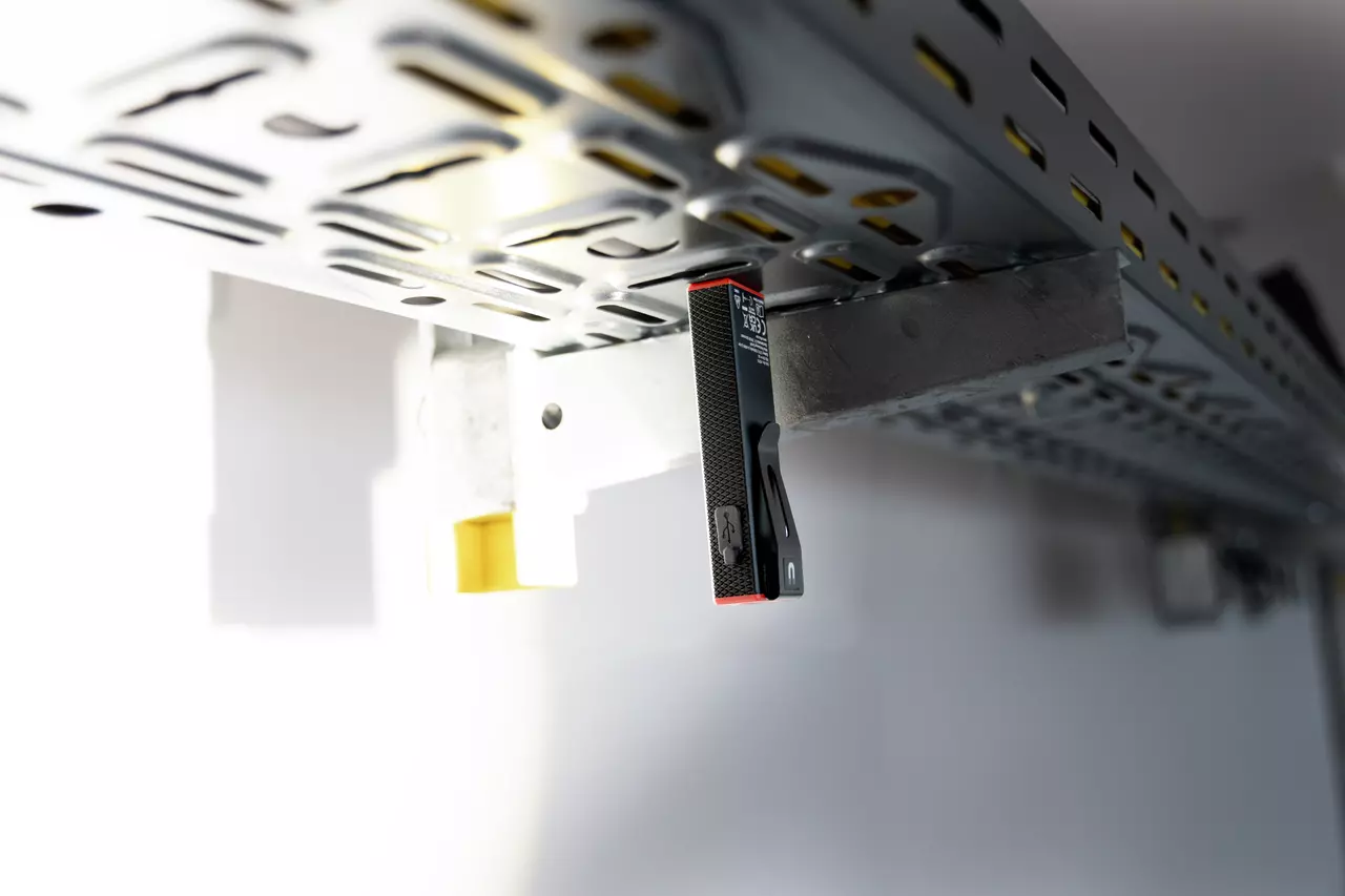 A small black and red magnetic handlight attached to a metal grid panel ceiling.