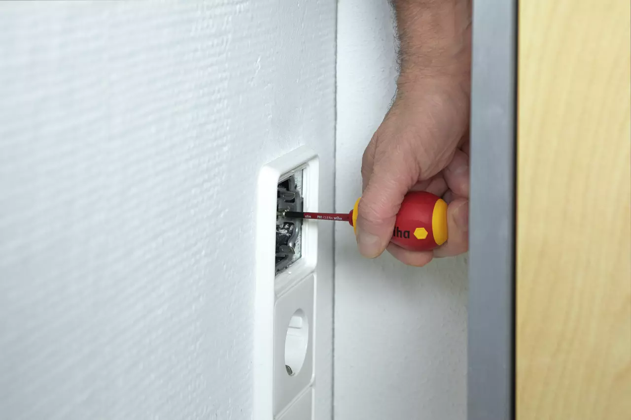 A person using a red and yellow screwdriver to work on a wall socket