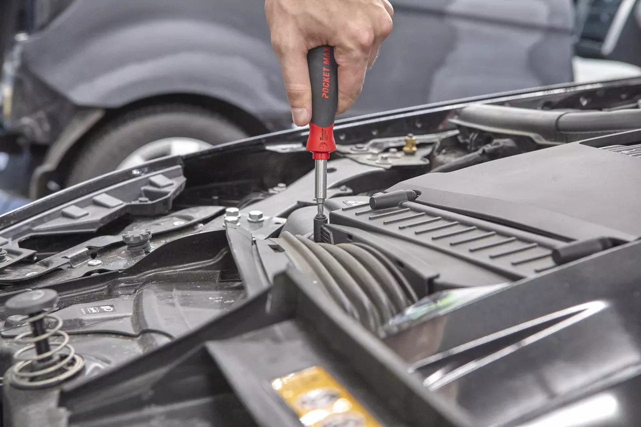 A person uses a screwdriver in a car engine compartment.