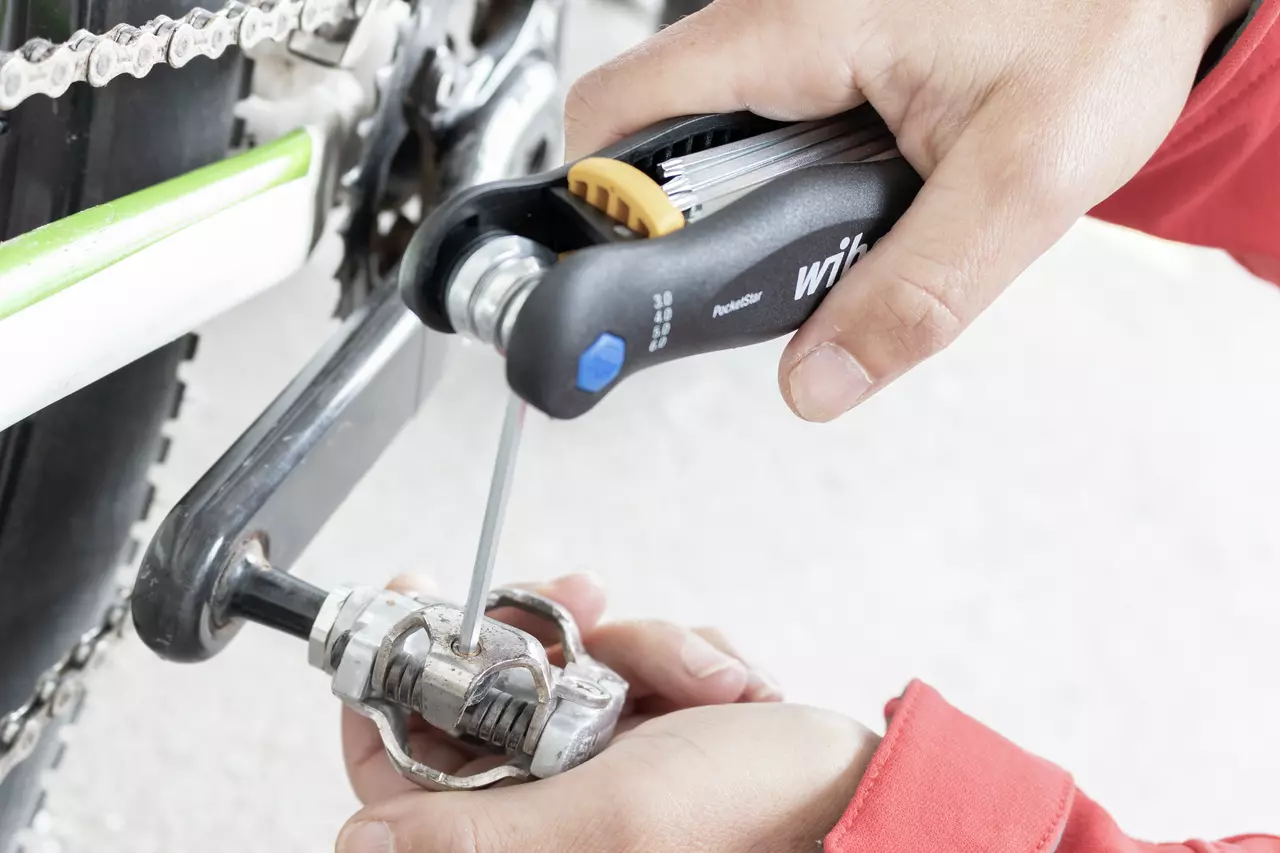 Person using a folding hex key set on a bicycle pedal