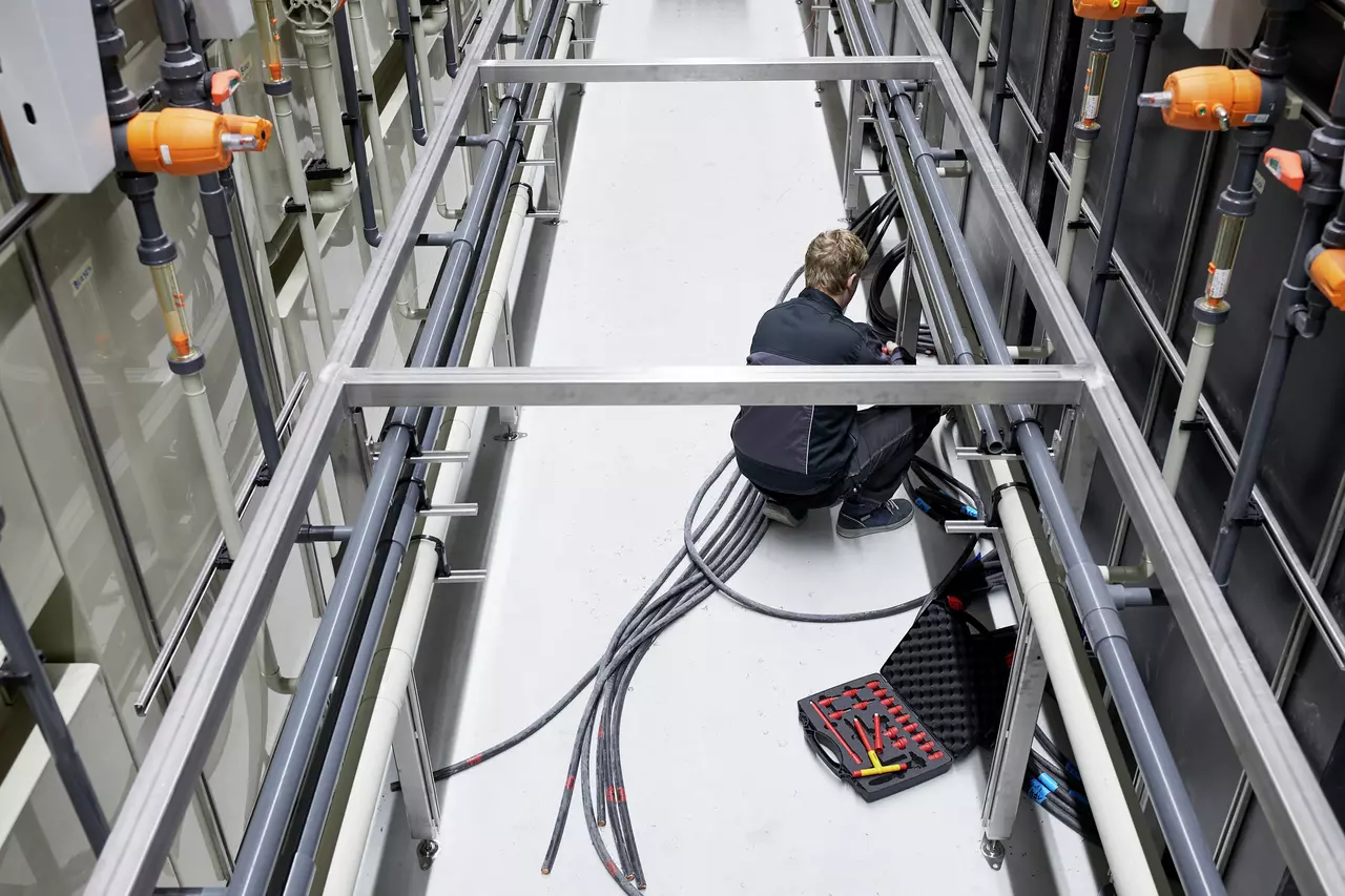 Person working with cables in industrial setting, tool set open on floor.