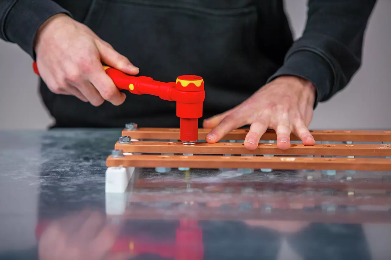 A person uses a red torque wrench on a metal bar secured with bolts.
