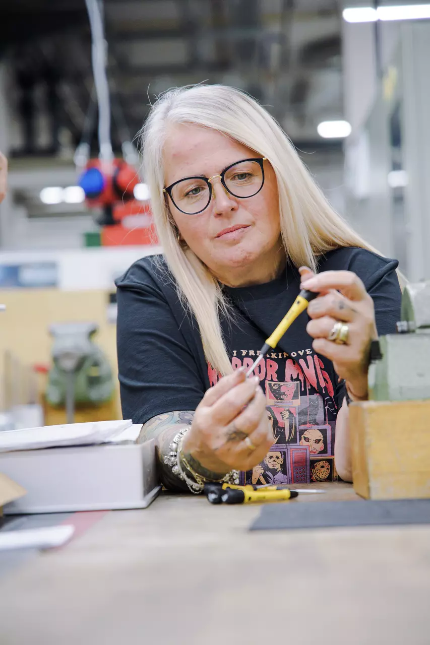 A person is holding and examining a yellow screwdriver at a table.