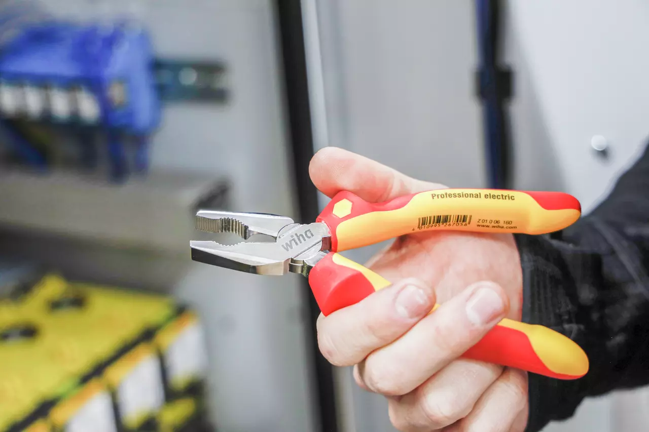 A person holding a red and yellow insulated combination plier marked "Professional electric".